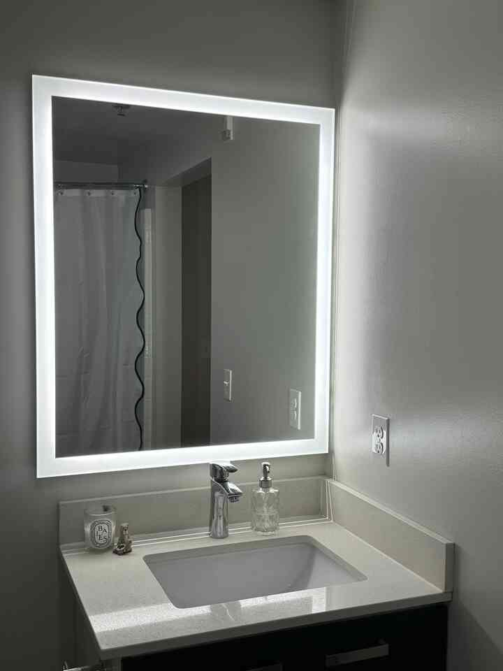 White-toned bathroom featuring a clean sink and illuminated mirror reflecting a modern space