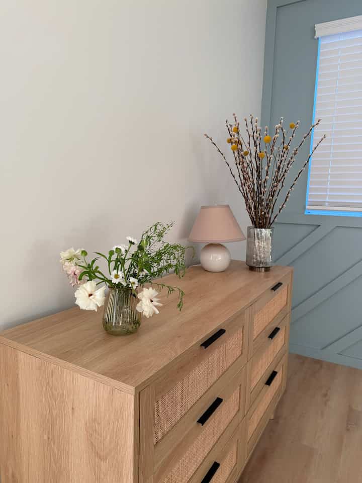 Natural wood-tone dresser topped with vases and beige table lamp in a simple, calming Japandi style space