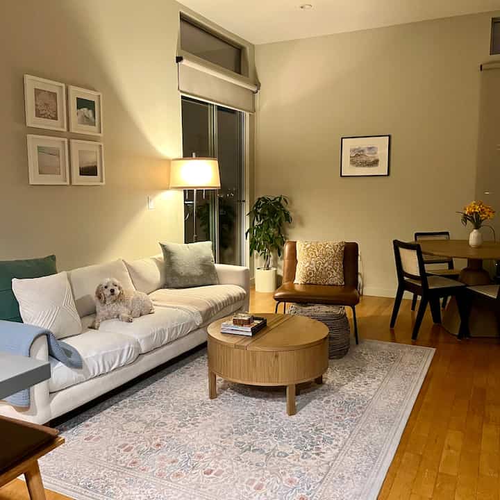 Wood tone living room featuring white sofa and leather armchair, warm lighting creating a cozy atmosphere