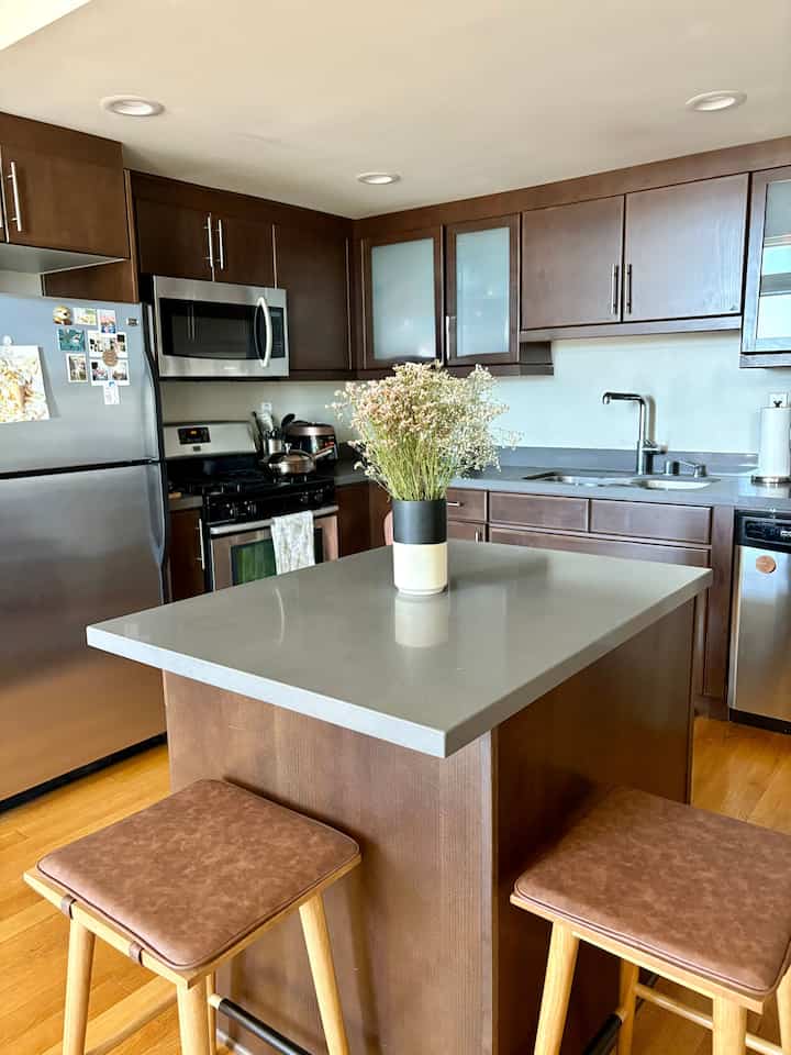 Warm brown and natural color kitchen featuring a kitchen island with a vase of wildflowers and bar stools, creating a cozy space