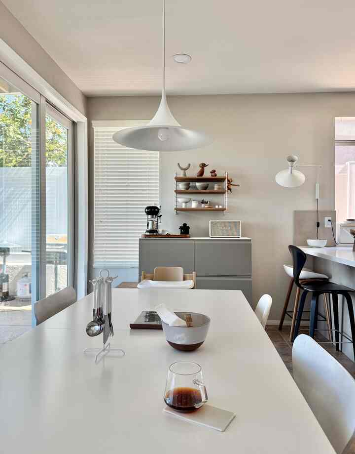 A white and natural color toned dining room featuring a large dining table, chairs, and a pendant light creating a cozy atmosphere