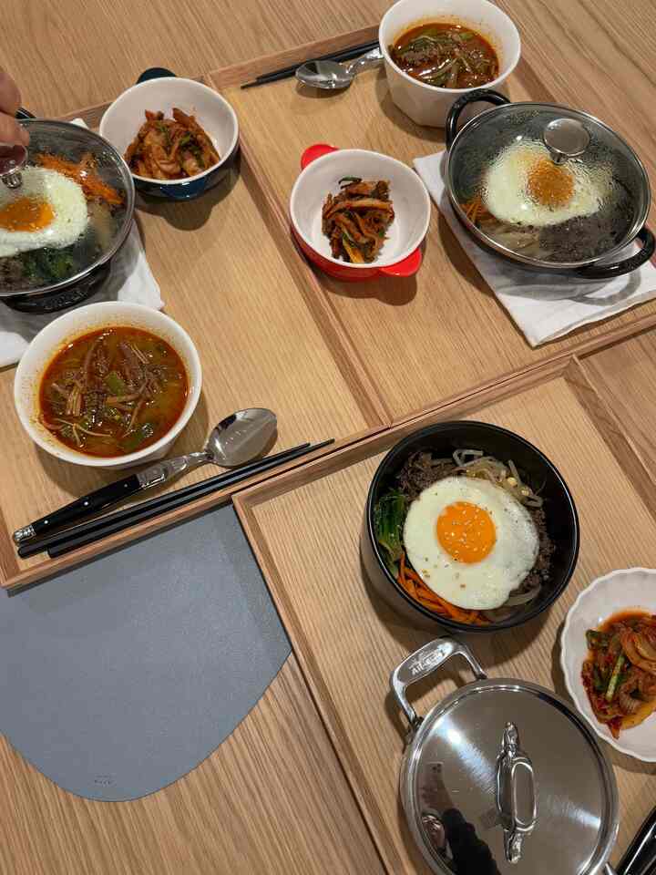 Warm wood-toned dining table featuring bibimbap dishes with kimchi and soups in a neat Korean meal setting