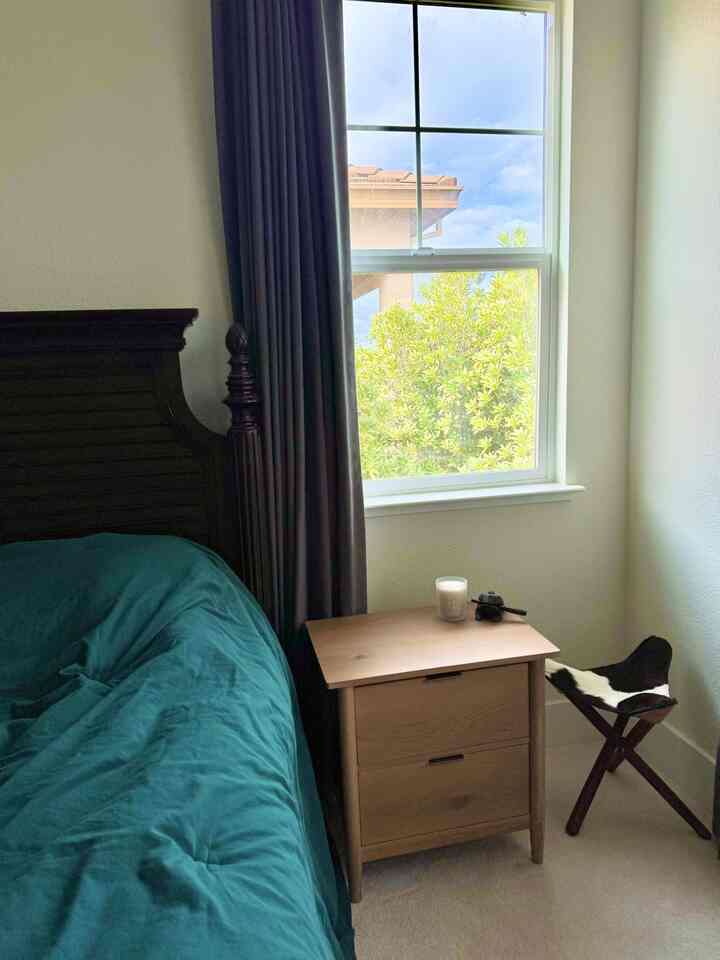 Green-toned bedroom featuring wood tone nightstand and dark bed with a warm atmosphere