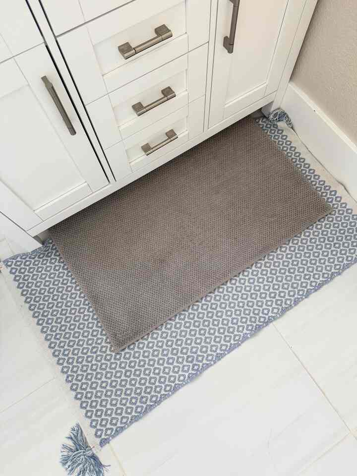 Bathroom with white cabinet and layered gray and blue patterned rugs placed on the floor