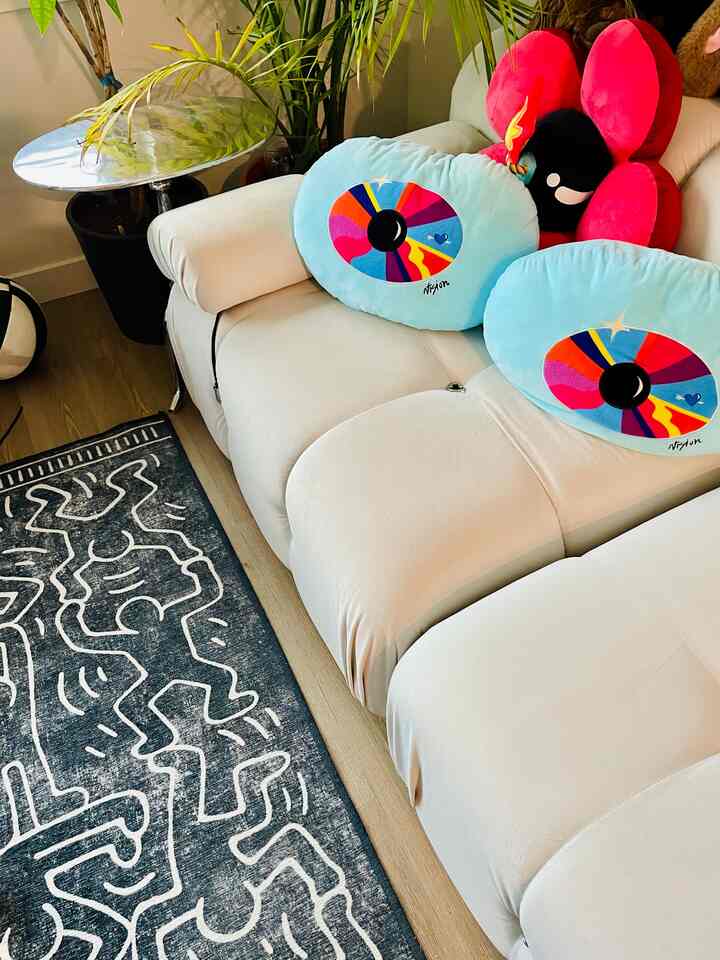 Bright white and light brown wood tone living room corner featuring a sectional sofa with pop art cushions and a Keith Haring rug, creating a cozy atmosphere