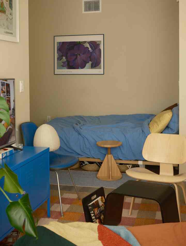 A cozy small studio bedroom with beige walls and blue bedding, featuring natural wood furniture arranged harmoniously