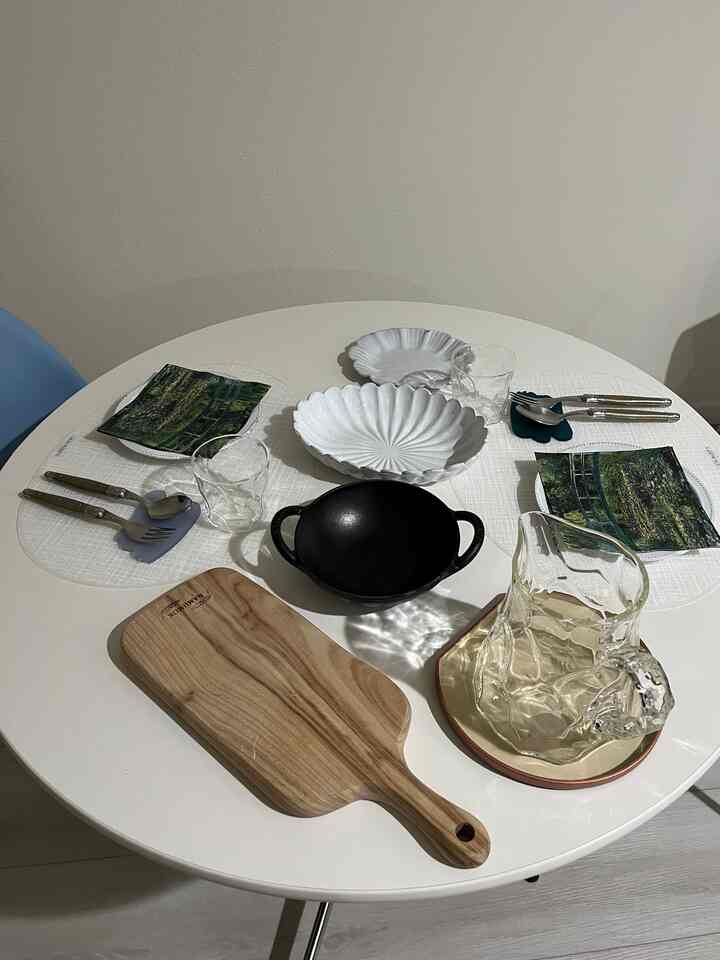 White and wood tone kitchen with a round dining table featuring various plates, cutlery, and a cutting board arranged neatly in a cozy setting