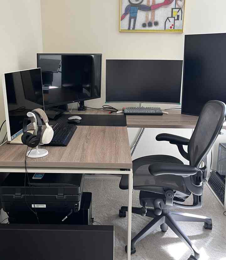 Wood-tone desks with black office chair and multiple monitors in a compact home office space