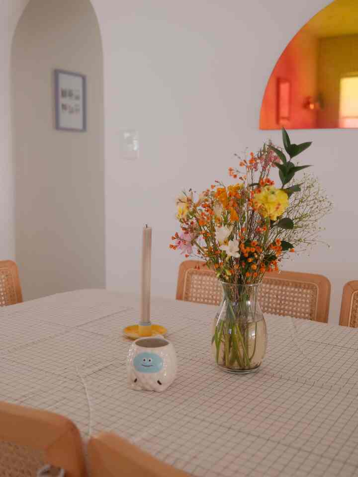 Natural-toned dining room featuring wood dining chairs and a checkered tablecloth with a flower vase and candle, creating a cozy atmosphere