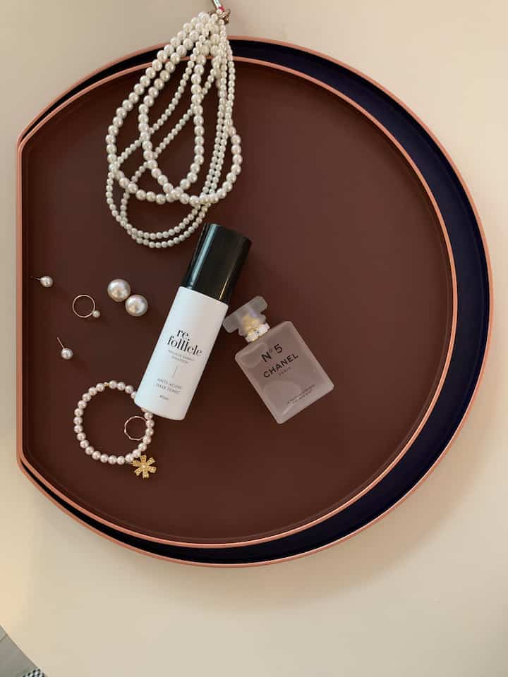 A stylish arrangement of pearl accessories and Chanel perfume on brown and navy half-moon trays in a beauty item setting