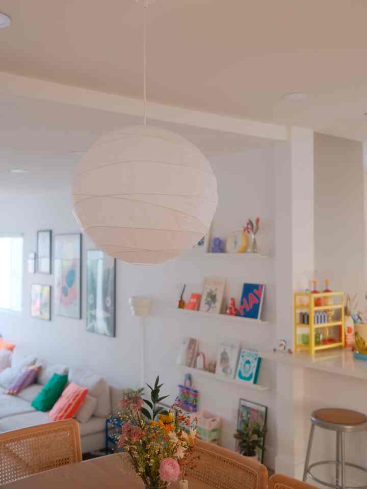 A simple living room in white and natural wood tones featuring a central Ikea Legolit paper pendant light shade