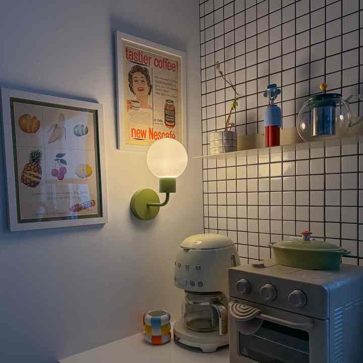 White and green toned kitchen corner featuring a vintage coffee machine, retro posters, and wall sconce creating a cozy home cafe atmosphere