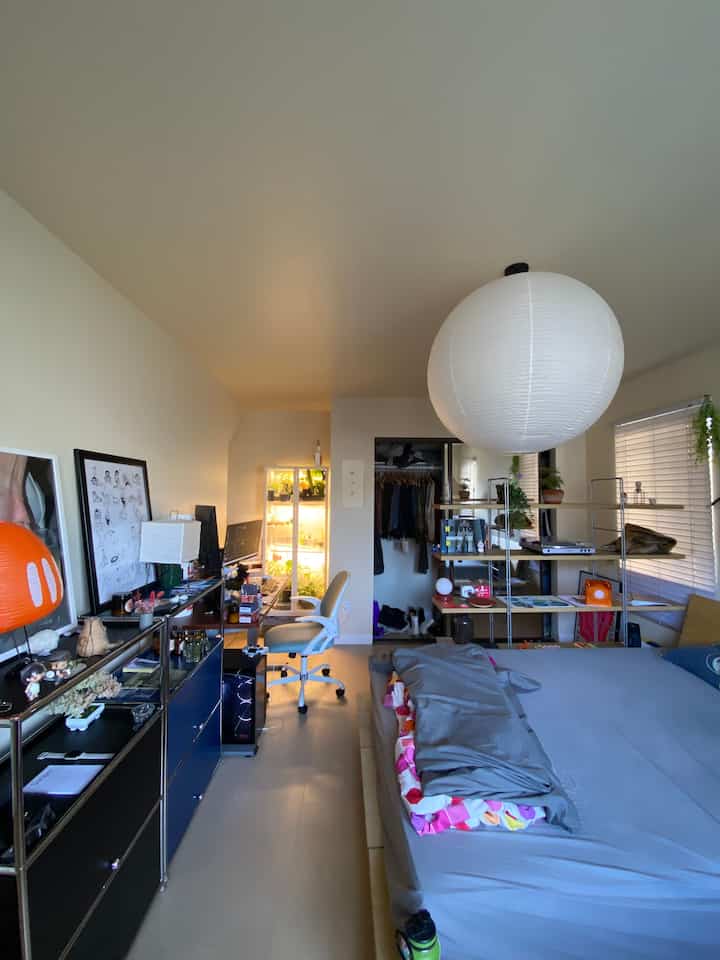 White dominant small bedroom featuring desk, storage units, and orange accent lamp creating a home office and sleeping space