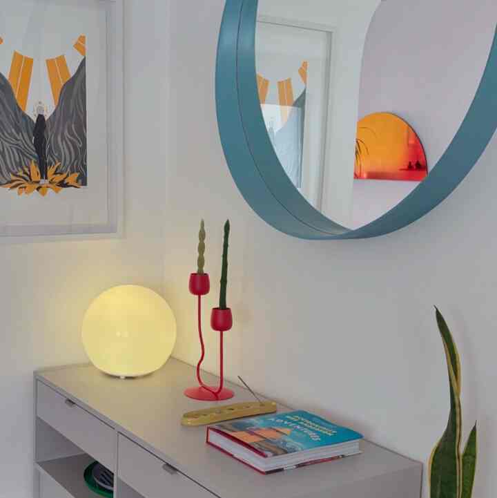 Minimal entrance space with light gray console table featuring a round white table lamp and red candlesticks