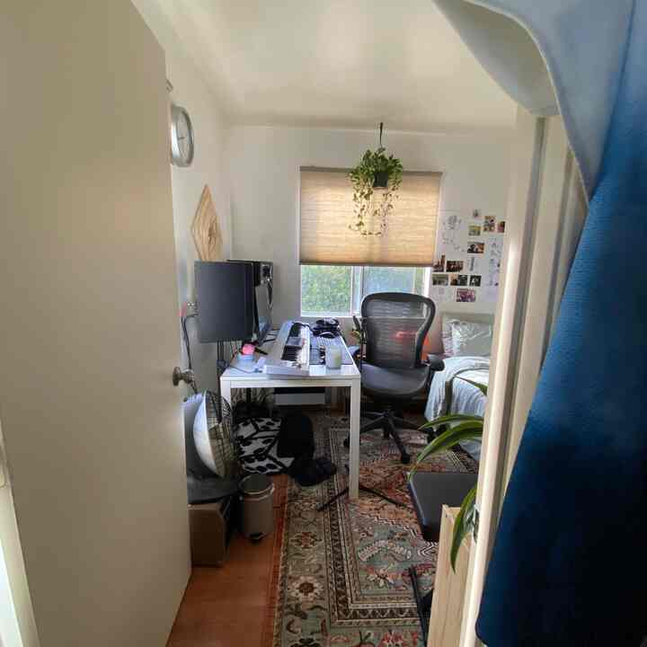 Beige-toned blinds light a compact home office and guest room space featuring a desk and office chair in a functional layout