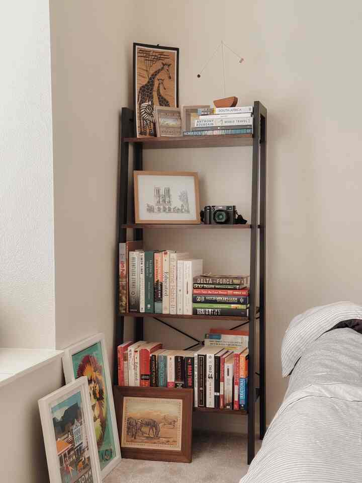 Ivory-toned bedroom with wooden bookshelf featuring multiple travel art frames creating a cozy nook