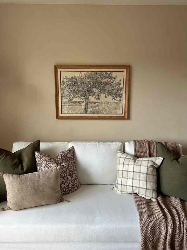 Beige-toned wall living room featuring a white sofa adorned with various cushions and a knitted throw, creating a cozy atmosphere