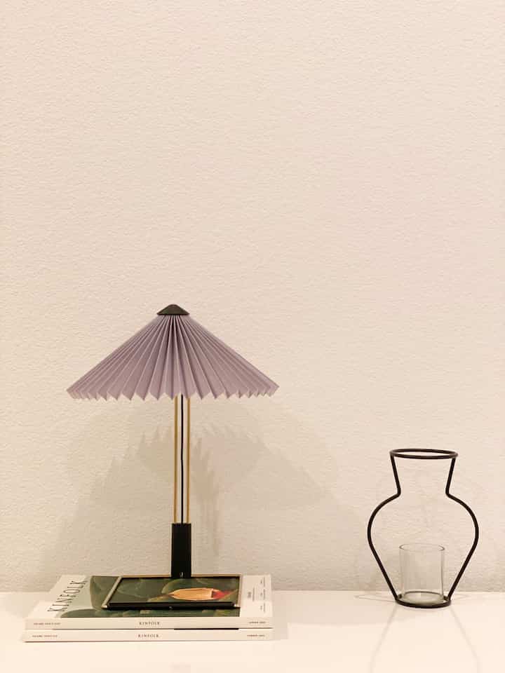 Minimal bedroom with lavender-toned table lamp and wire vase placed neatly on a white dresser