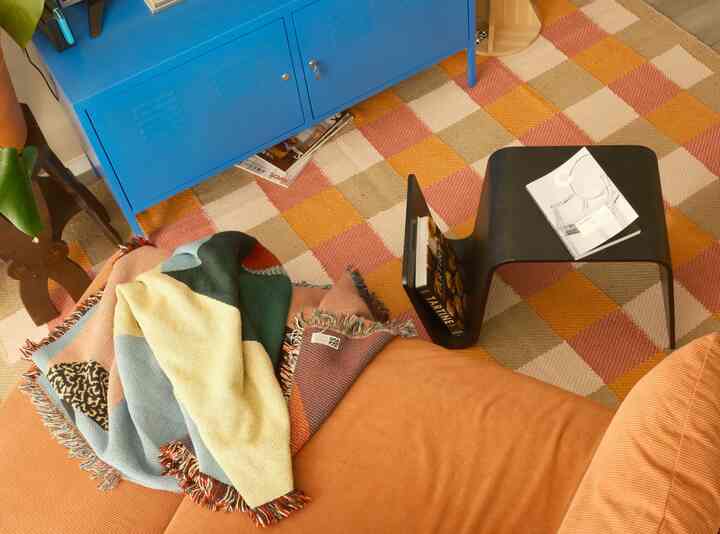 Orange and blue toned living space featuring a sofa, checkered rug, and black side table creating a cozy atmosphere