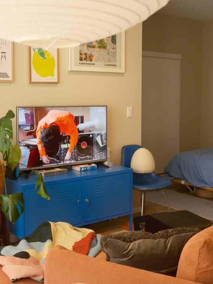 Warm beige-toned living room with blue TV stand, orange sofa, and visible bedroom area creating cozy interior