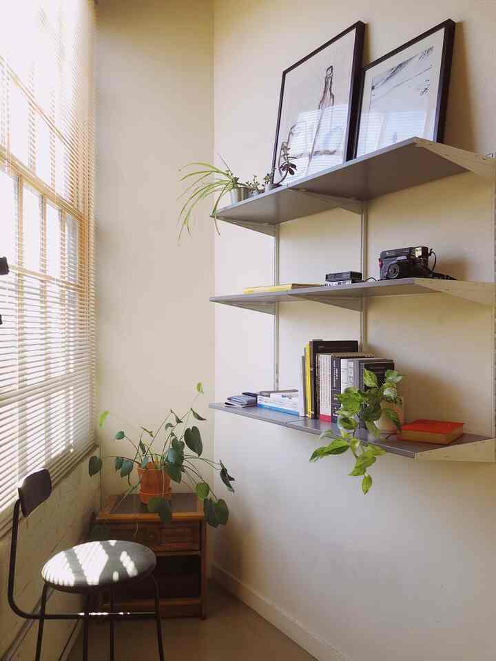Warm beige-toned reading nook by window with wooden side table, wall shelves, and plants creating a natural atmosphere