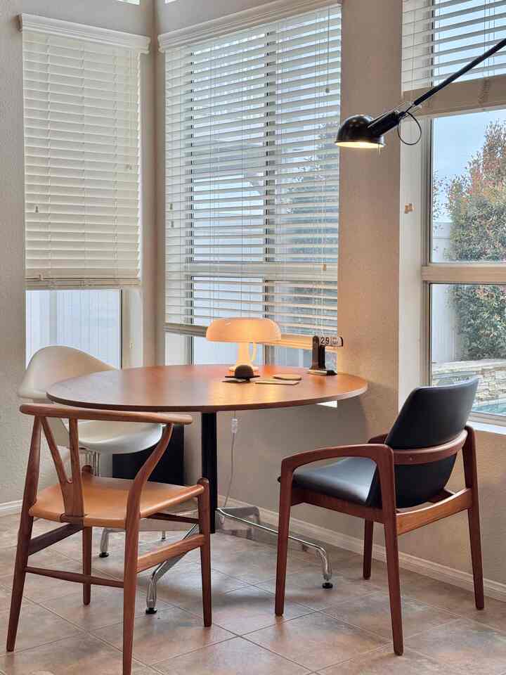 Beige-walled dining room with large windows, featuring a round dining table and Nordic-style chairs in a cozy setting