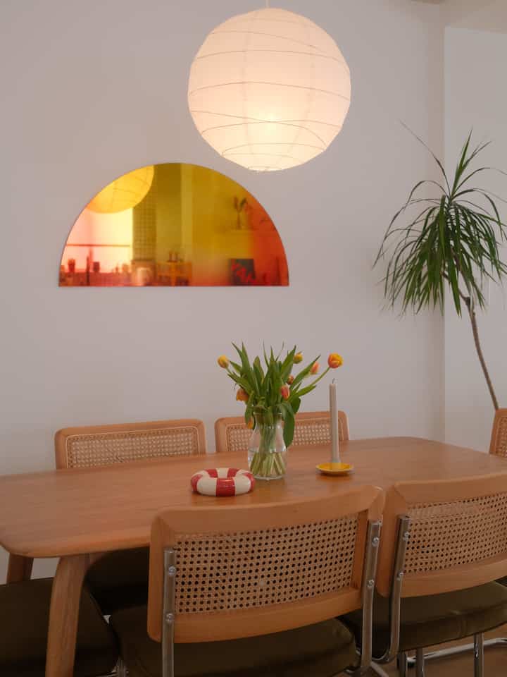 Natural wood tone and white-walled dining room for four, featuring tulip bouquet and candle on table creating cozy atmosphere