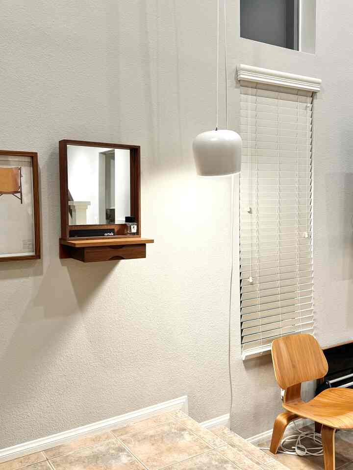 White-walled entrance space featuring wood-tone furniture and vintage style pendant lighting with a clean, warm atmosphere