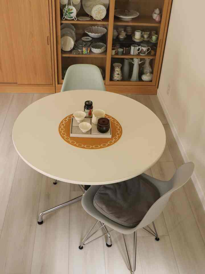 White and wood tone living room dining space featuring a round table with chairs and a tea set, creating a warm atmosphere