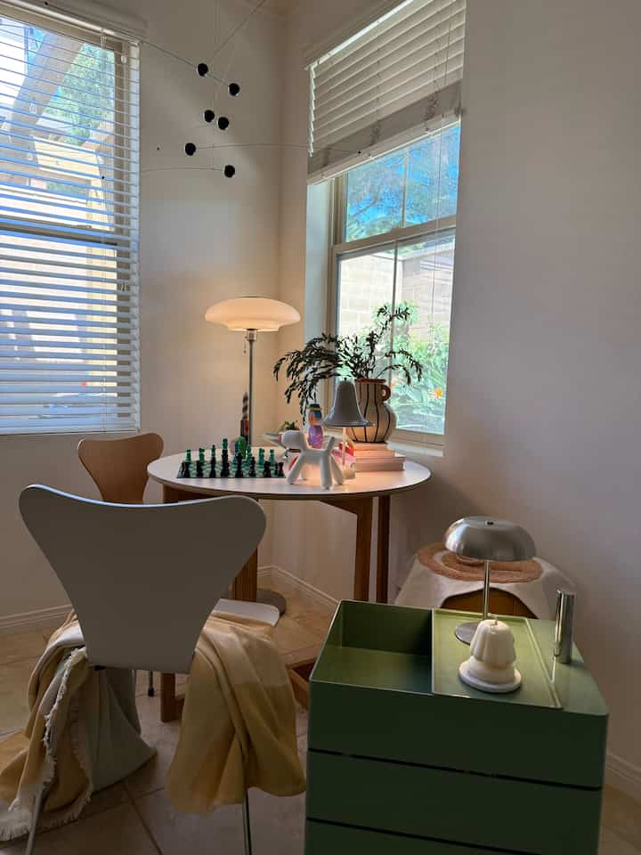 Beige-toned Mid-Century Modern dining space with wooden table and chairs, floor lamp, and vase near window in a cozy room