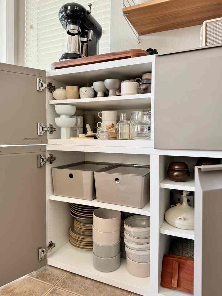 White and beige tone kitchen cabinet featuring a semi-automatic coffee machine and neatly organized bowls, creating a tidy kitchen space