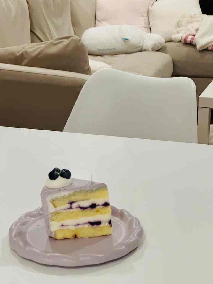 Beige and white toned living room featuring a white dining table with a slice of blueberry cake on a lavender plate, creating a cozy atmosphere