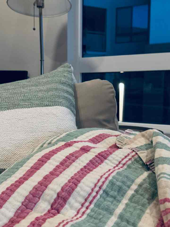 Natural-toned living room space with beige sofa, featuring green and white cushions and a striped throw blanket creating a cozy atmosphere