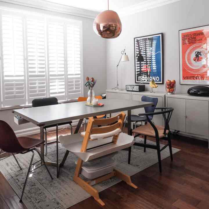 A modern dining room with white and wood tones, featuring six diverse chairs around a dining table and vintage posters on the wall