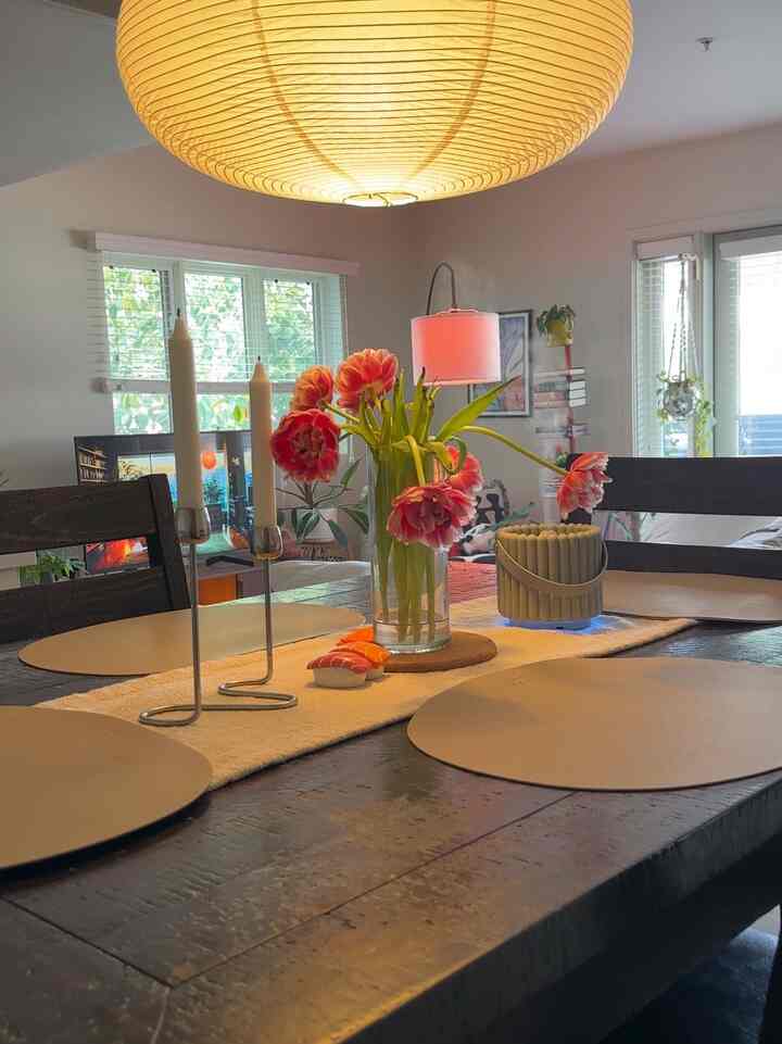 Natural-toned dining room centered on dark wood table under warm yellow pendant light, decorated with flowers and candles for a cozy feel