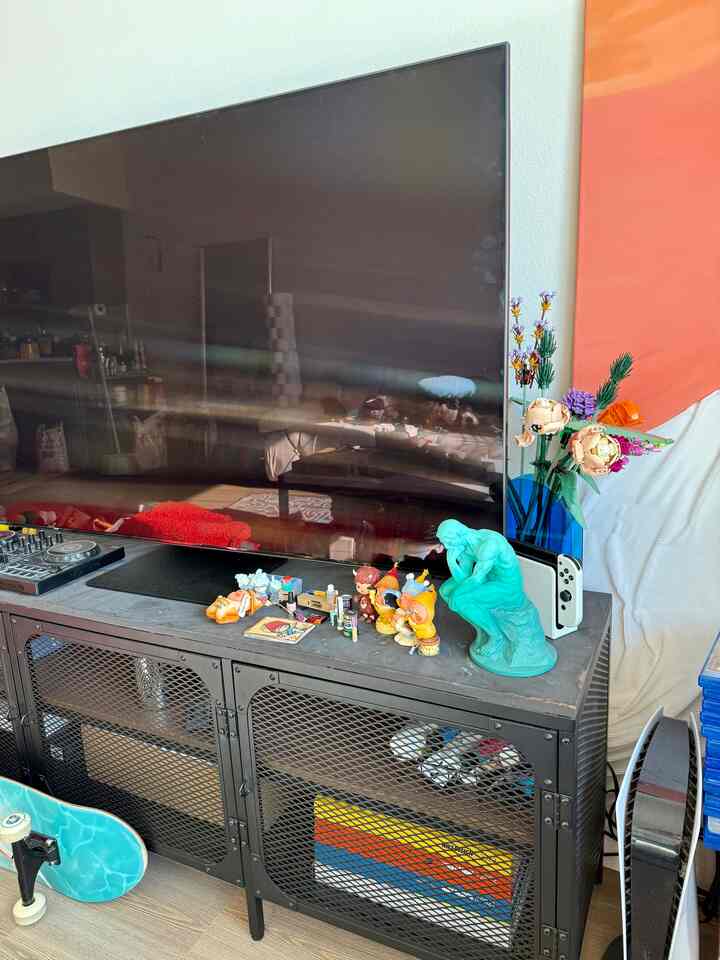 Black metal shelf with various mini toys, a Nintendo Switch, and large TV in a living room space