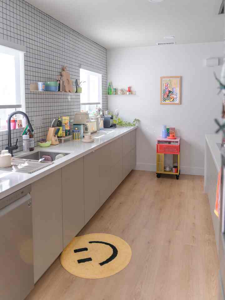 Bright kitchen featuring white walls and wood tone flooring, with a colorful kitchen cart and smile face bath mat for a clean interior
