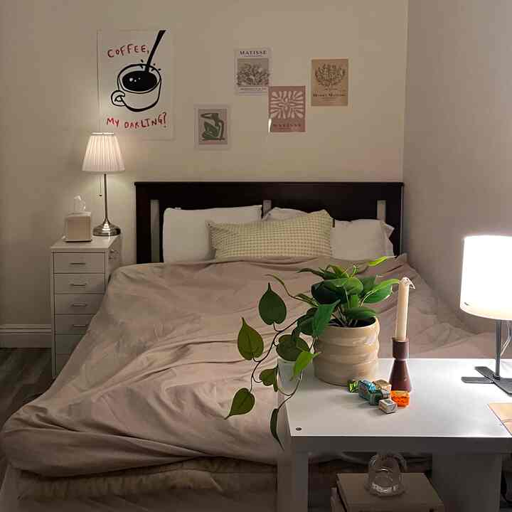 Warm beige-toned bedroom featuring a central bed flanked by nightstands, a table with plants and lamps, creating a cozy atmosphere