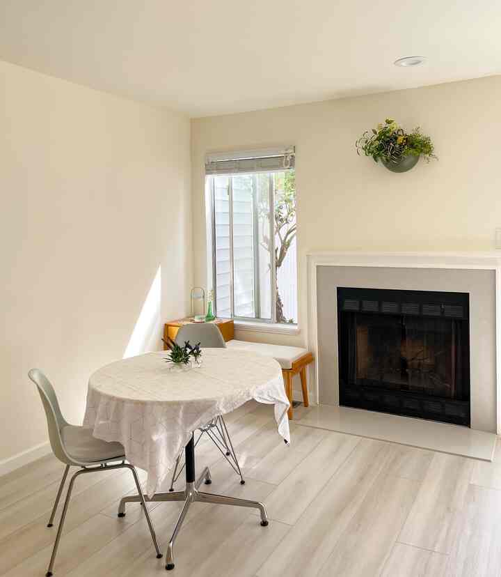 White and natural toned kitchen space featuring a round dining table with chairs and a fireplace in a simple interior