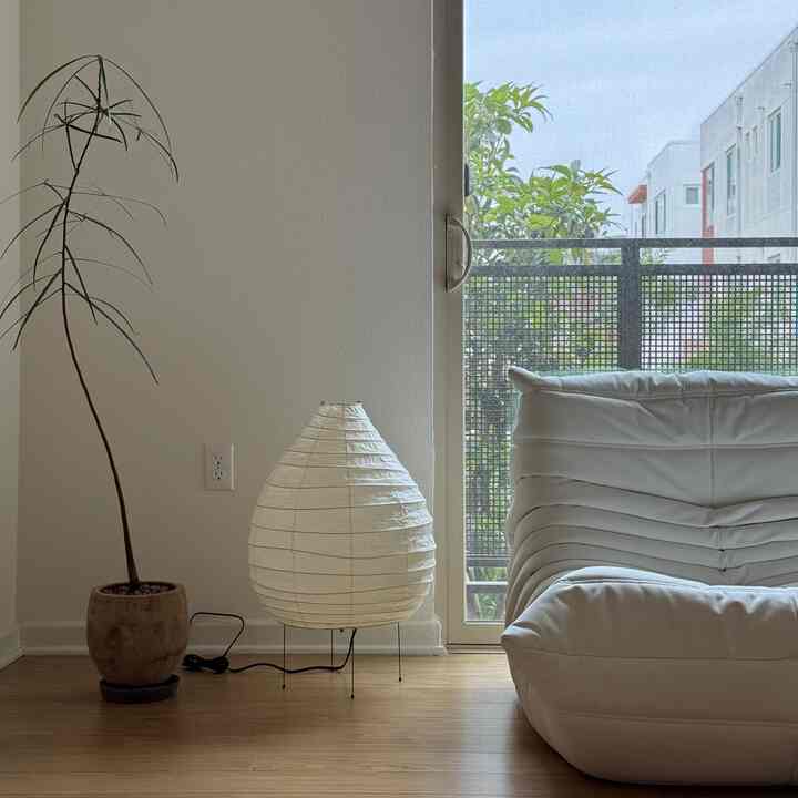 Natural tone living room with wood floor and white armchair featuring a floor lamp and balcony view