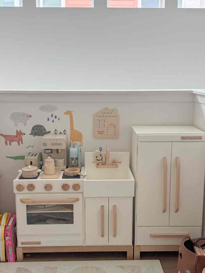 Natural toned kids' play kitchen space with white and wood toy kitchen and refrigerator arranged neatly