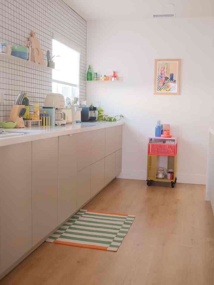 Bright kitchen space with white walls and wood tone flooring, featuring beige cabinets and a colorful kitchen cart