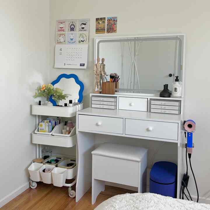 White and natural toned bedroom vanity area featuring a storage trolley and large mirror with a clean atmosphere