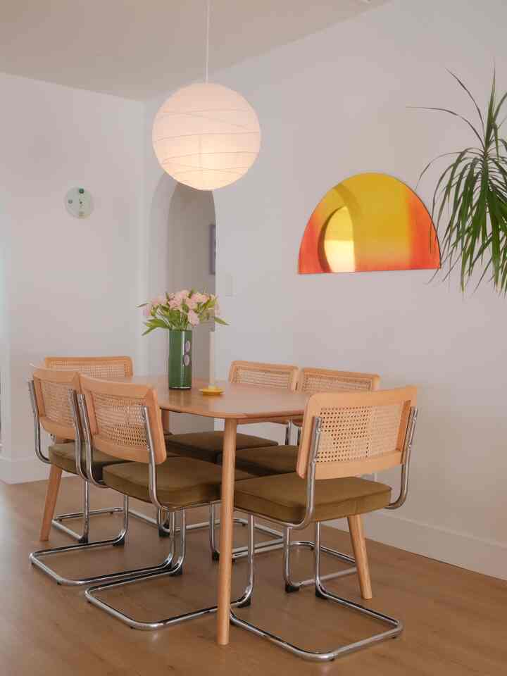 Natural wood tones and white walls dining room featuring a central dining table with six rattan back chairs creating a cozy space