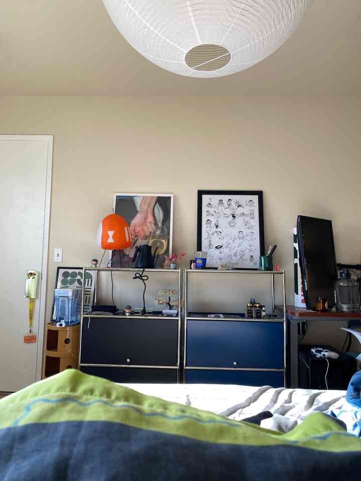 A modern home office featuring light beige walls and white ceiling light, centrally placed blue and black storage cabinets with an orange lamp accent