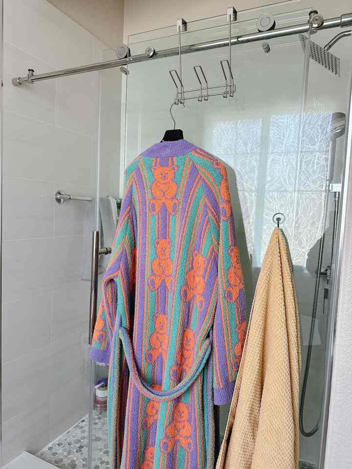 Bright bathroom with white tiles and beige towel, featuring a colorful bathrobe hanging centrally, creating a cozy atmosphere