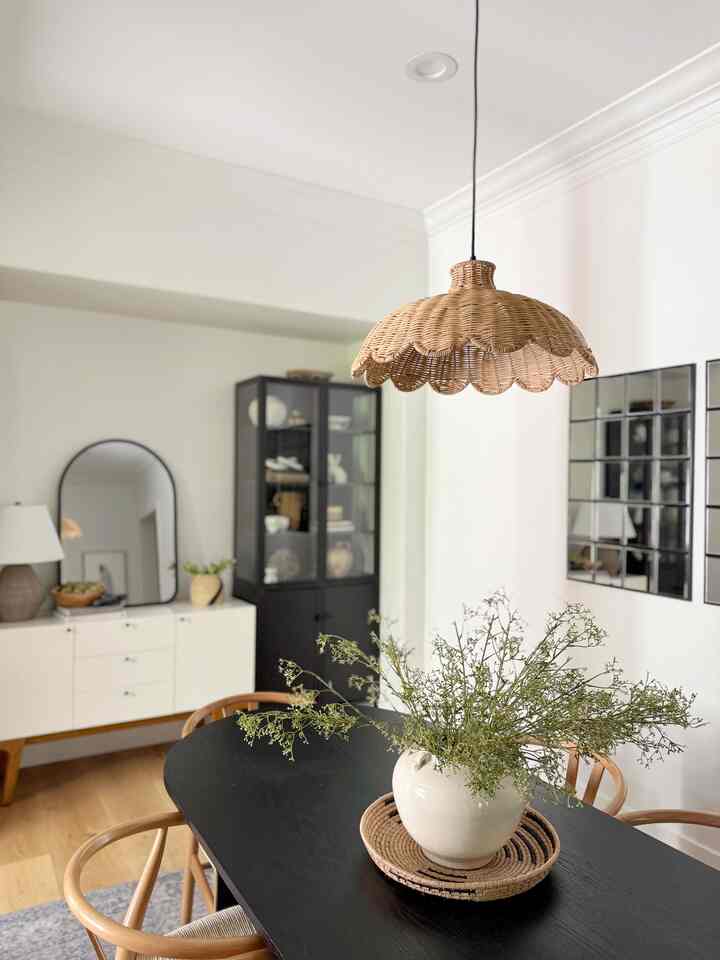 Modern dining room with natural wood tones and black furniture featuring a central dining table and woven pendant light