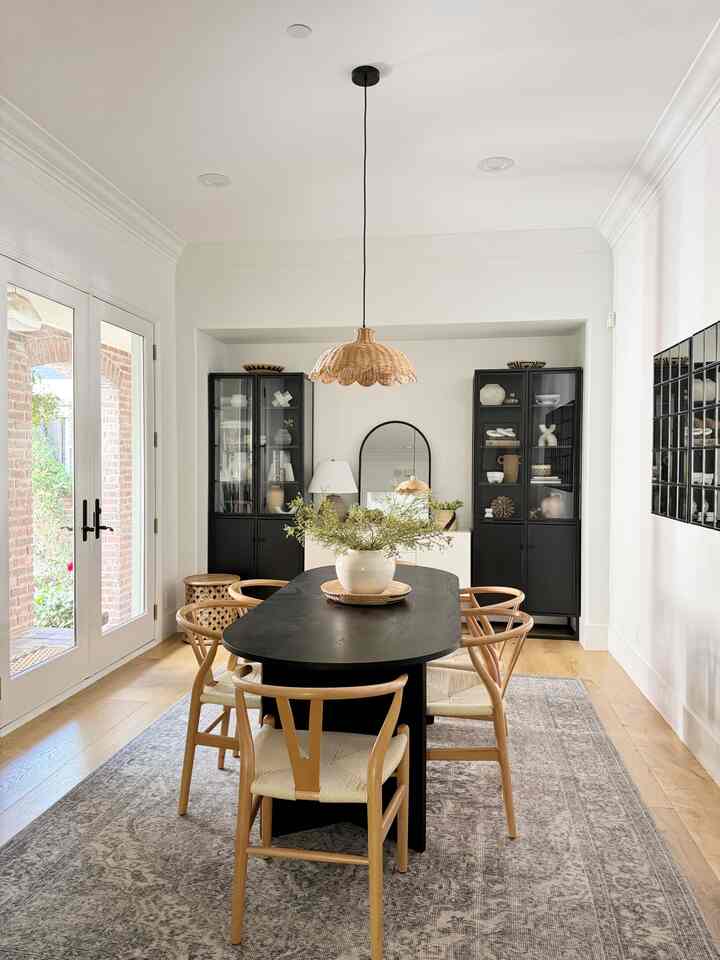 Modern dining room with white walls and wood tones featuring a central black oval dining table and natural wood chairs