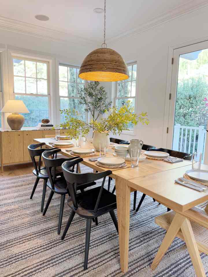 A bright, modern dining room with natural wood tones and white walls, featuring a large dining table and black dining chairs
