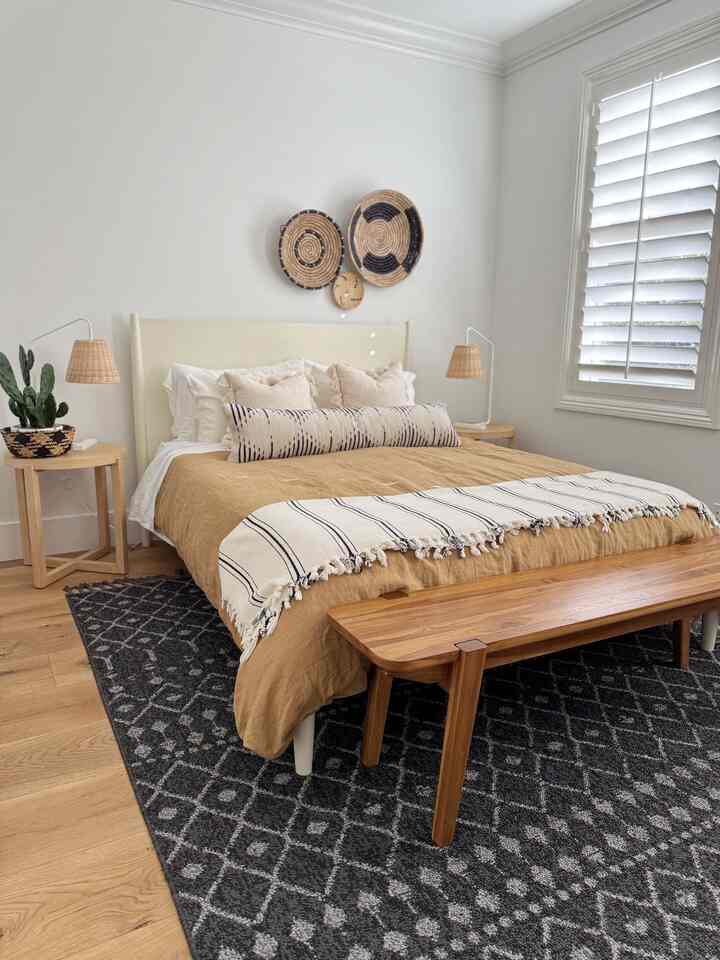 Natural color and wood tone bohemian bedroom featuring bedding, rug, nightstands, and woven wall decor creating a cozy atmosphere